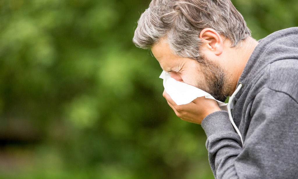 man with allergy or infection sneezing into tissue