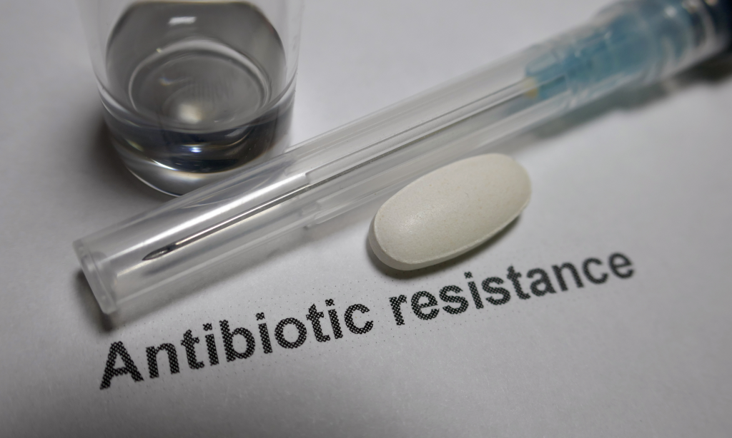 glass of water, needle and a pill on a white background with words antibiotic resistance