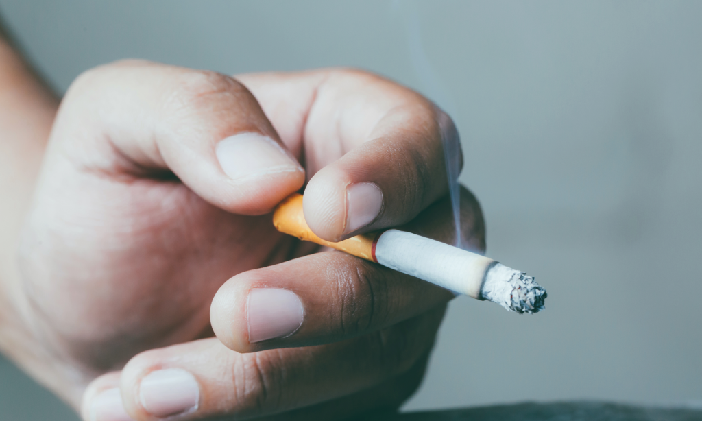 hand resting on table with lit cigarette between fingers