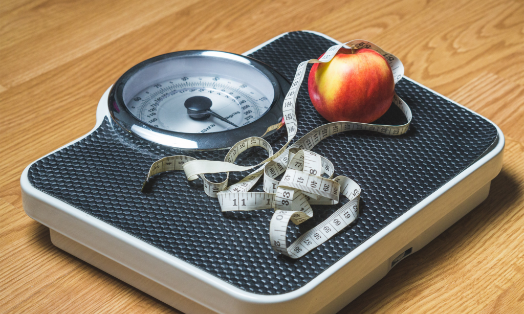 scales on wooden floor with apple and tape measure on top of it