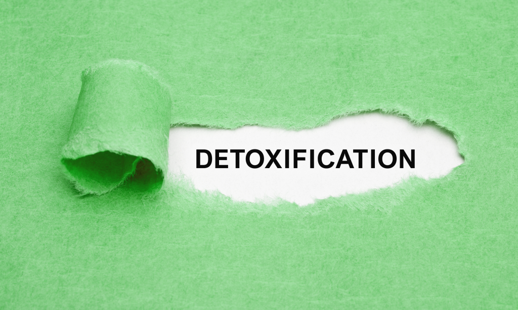 green paper with a small piece ripped to reveal the word detoxification written in black font on white paper